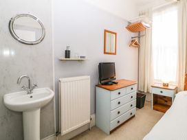 A bedroom corner with a sink and mirror a small chest of drawers with a TV on top and a bedside table with a lamp at Midhurst in Brixham