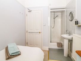 A small bedroom with a bed and folded towels next to a white door and an en suite bathroom with a shower and sink at Midhurst in Brixham