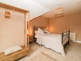 A bedroom with a bed covered in quilted bedding a wooden nightstand a hanging rack with hangers and a pillow on the bench at Midhurst in Brixham