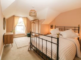 A bedroom with a bed a wooden dresser a window with curtains and a hanging light at Midhurst in Brixham