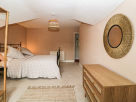 A bedroom with a bed covered with a quilt and pillows a woven rug a dresser and a round mirror at Midhurst in Brixham