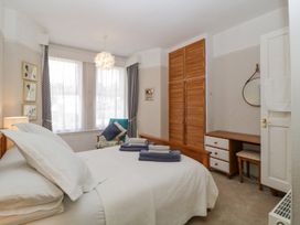 A bedroom with a bed with white bedding folded towels on top a wooden wardrobe a wooden desk with drawers and a chair and a blue armchair near a window with curtains at Midhurst in Brixham