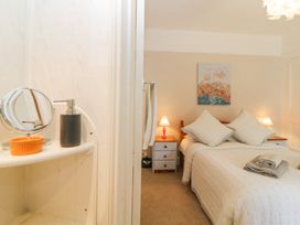 A bedroom with a double bed, two pillows, folded towels on the bed, two bedside tables with lamps, a colorful painting on the wall, and a bathroom shelf with a mirror and soap dispenser at Midhurst in Brixham