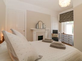 A bedroom with a bed, pillows, folded towels, a fireplace with a mirror, a chair with a cushion, and a dresser under a window at Midhurst in Brixham