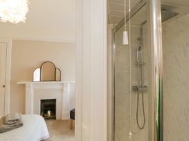 A bedroom with a white bed and folded towels next to a fireplace with a three-part mirror and a bathroom shower with a silver frame in Midhurst Brixham