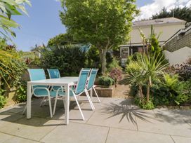 A garden patio with a white table and four blue chairs surrounded by plants and trees at Midhurst in Brixham