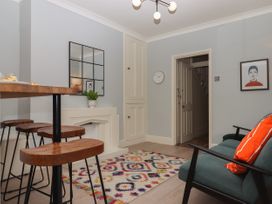 A room with wooden bar stools a colorful rug a green sofa with orange pillows and a wall clock at Midhurst in Brixham