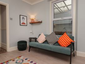 A sitting area with a green sofa with cushions a dark green round ottoman a small side table a wall shelf with a lamp and decoration and a framed picture on the wall at Midhurst in Brixham