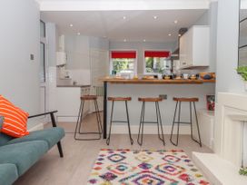 A kitchen with four wooden stools at a breakfast bar and a colorful rug in front of a green sofa at Midhurst in Brixham