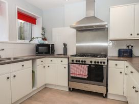 A kitchen with white cabinets a stainless steel oven microwave and a window with a red blind at Midhurst in Brixham