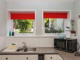 A kitchen sink with a dish rack and soap bottles next to two windows with red blinds and a microwave with teapots on top at Midhurst in Brixham
