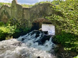 A bridge over a stream with rocks and ferns at Beechcroft Cottage, North Molton