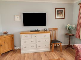 A living room with furniture including a television and wooden chair at Bro Mebyd, Criccieth