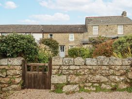 An outdoor view of a stone wall and wooden gate with a house and plants at 3 The Green