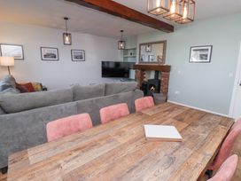 A living and dining room with a wooden table and pink chairs a gray sofa a television and a fireplace at The Old School in Lowick