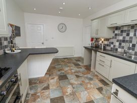 A kitchen with tiled floor white cabinets black countertops a wall clock and a bottle with glasses on the counter at The Old School in Lowick