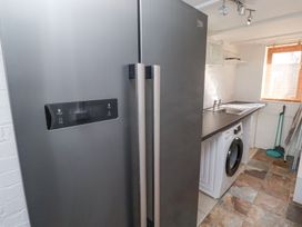 A utility room with a gray fridge freezer stainless steel sink washing machine and cleaning tools at The Old School in Lowick