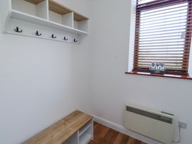A small room with a wooden bench with cubby holes a wall-mounted shelf with hooks and a window with wooden blinds and a flower pot at The Old School in Lowick