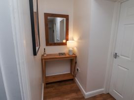 A hallway corner with a wooden console table holding a lamp, a bell, and a notebook under a wooden framed mirror at The Old School in Lowick