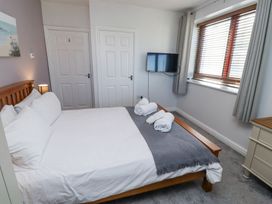 A bedroom with a wooden bed and white bedding beside two white doors and a wall-mounted TV at The Old School in Lowick