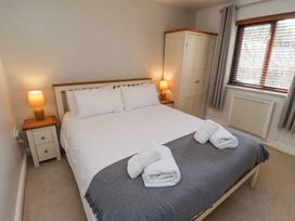 A bedroom with a bed with white sheets and gray blanket with two folded towels on top two bedside tables with lamps a white wardrobe and a window with blinds and curtains at The Old School in Lowick