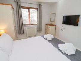 A bedroom with a bed towels on the floor a chest of drawers a wall-mounted TV and a window with curtains at The Old School in Lowick