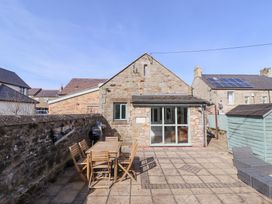 A stone house with a patio featuring a wooden table and chairs a barbecue and a garden shed at The Old School in Lowick