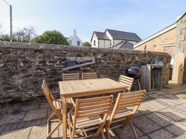 An outdoor patio area with a wooden table and six chairs a barbecue and a stone wall at The Old School in Lowick