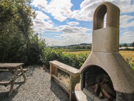 An outdoor fireplace and wooden seating area in a garden at Aston - Shepherd Hut Aston On Clun
