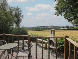 An outdoor patio with a table and chairs overlooking a landscape at Aston - Shepherd Hut Aston On Clun