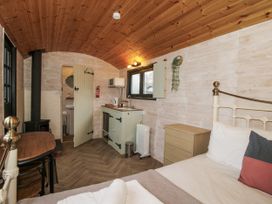 A bedroom with a bed, table, and kitchen unit at Aston - Shepherd Hut Aston On Clun
