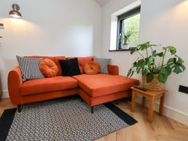A living room with an orange sofa and patterned cushions a wooden side table with a plant and a window at The Haven in Cloughton near Burniston