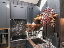 A kitchen with dark cabinets a black stove a toaster kettle and a plant on a wooden shelf at The Haven in Cloughton near Burniston