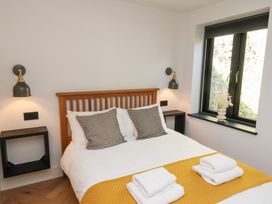 A bedroom with a wooden bed frame two patterned pillows two wall lamps and a window with a vase on the sill at The Haven Cloughton near Burniston