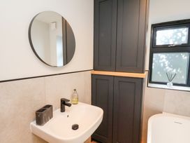 A bathroom sink with a round mirror above and a tall dark cabinet next to a window at The Haven in Cloughton near Burniston