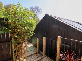 An outdoor area with a wooden trellis supporting plants gravel path and a black siding building with railing at The Haven in Cloughton near Burniston