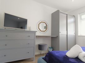 A bedroom with a grey dresser and TV a small stool an octagonal mirror a grey wardrobe and a bed with towels at 65 Channel View in Ilfracombe