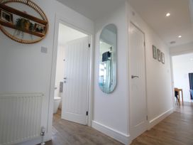 A hallway with wooden flooring white walls several doors a wall mirror and framed pictures at 65 Channel View in Ilfracombe