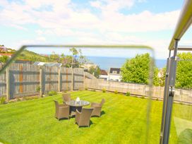 A backyard with a round glass table and four wicker chairs on grass with a wooden fence and an ocean view at 65 Channel View in Ilfracombe