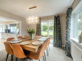 A dining room with a wooden table set with plates and orange chairs next to windows with patterned curtains at Broadsands in Paignton