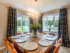 A dining room with a wooden table set with plates orange chairs and large windows with patterned curtains at Broadsands in Paignton