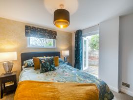 A bedroom with a bed with floral bedding two bedside tables with lamps window with a floral blind and door leading outside at Broadsands in Paignton