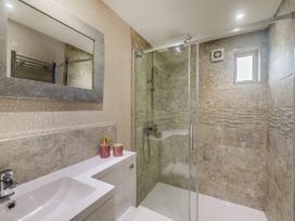 A bathroom with a sink, mirror, soap dispenser, and a glass shower enclosure with tiled walls at Broadsands in Paignton