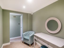 A small room with a blue armchair white desk and round mirror on a green wall at Broadsands in Paignton