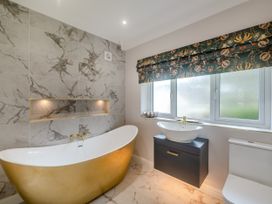 A bathroom with a gold bathtub a sink with a dark cabinet and a toilet at Broadsands in Paignton