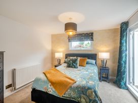 A bedroom with a bed with floral bedding and orange throw and pillows two bedside tables with lamps a chest of drawers and a window at Broadsands in Paignton