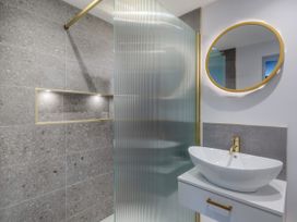 A bathroom with a white sink and gold faucet and mirror next to a shower with grey tiled wall at Broadsands in Paignton