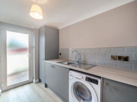 A utility room with a washing machine under a countertop and a sink next to a frosted glass door at Broadsands in Paignton
