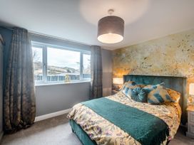A bedroom with a bed with green cushions and a floral duvet cover by a window with curtains at Broadsands in Paignton