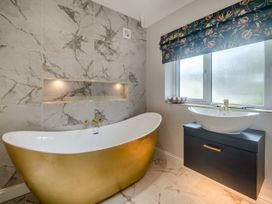 A bathroom with a gold bathtub a white sink on a black cabinet and a window with patterned blinds at Broadsands Paignton